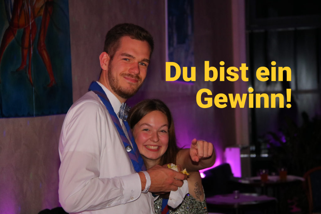 Zwei Pfadfinder*innen in Abendgarderobe mit Halstuch lächeln in die Kamera.