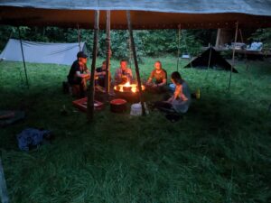 Gruppe von fünf Leuten sitzt im dunklen Zelt um ein Feuer herum