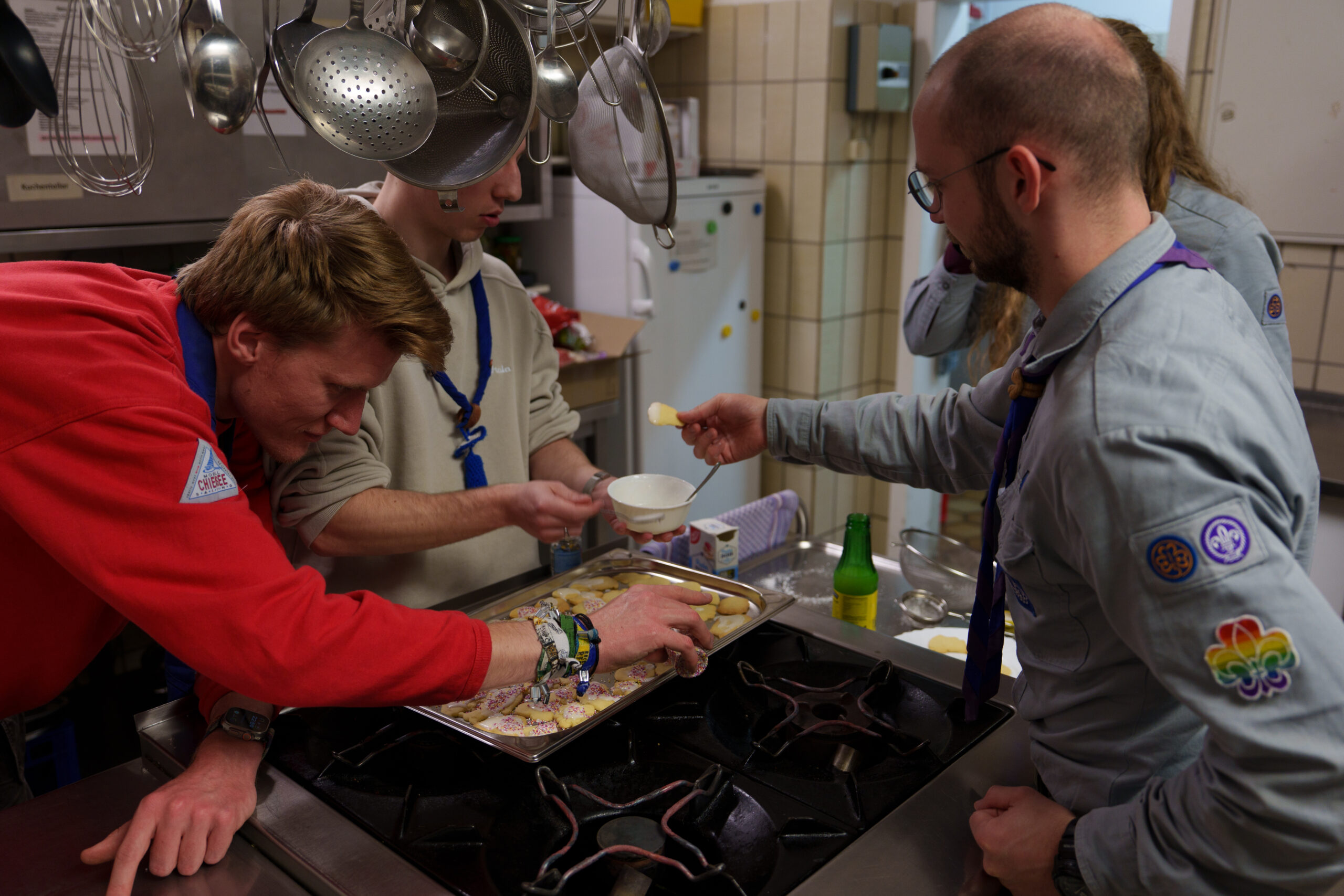 Vier Teilnehmer*innen stehen um einen Gasherd herum, auf dem ein Blech mit Keksen liegt, und verzieren diese.