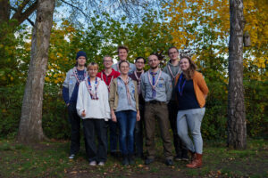 Die acht Teilnehmer*innen des Kurses stehen als Gruppe zusammen vor einer Hecke zwischen zwei Bäumen.