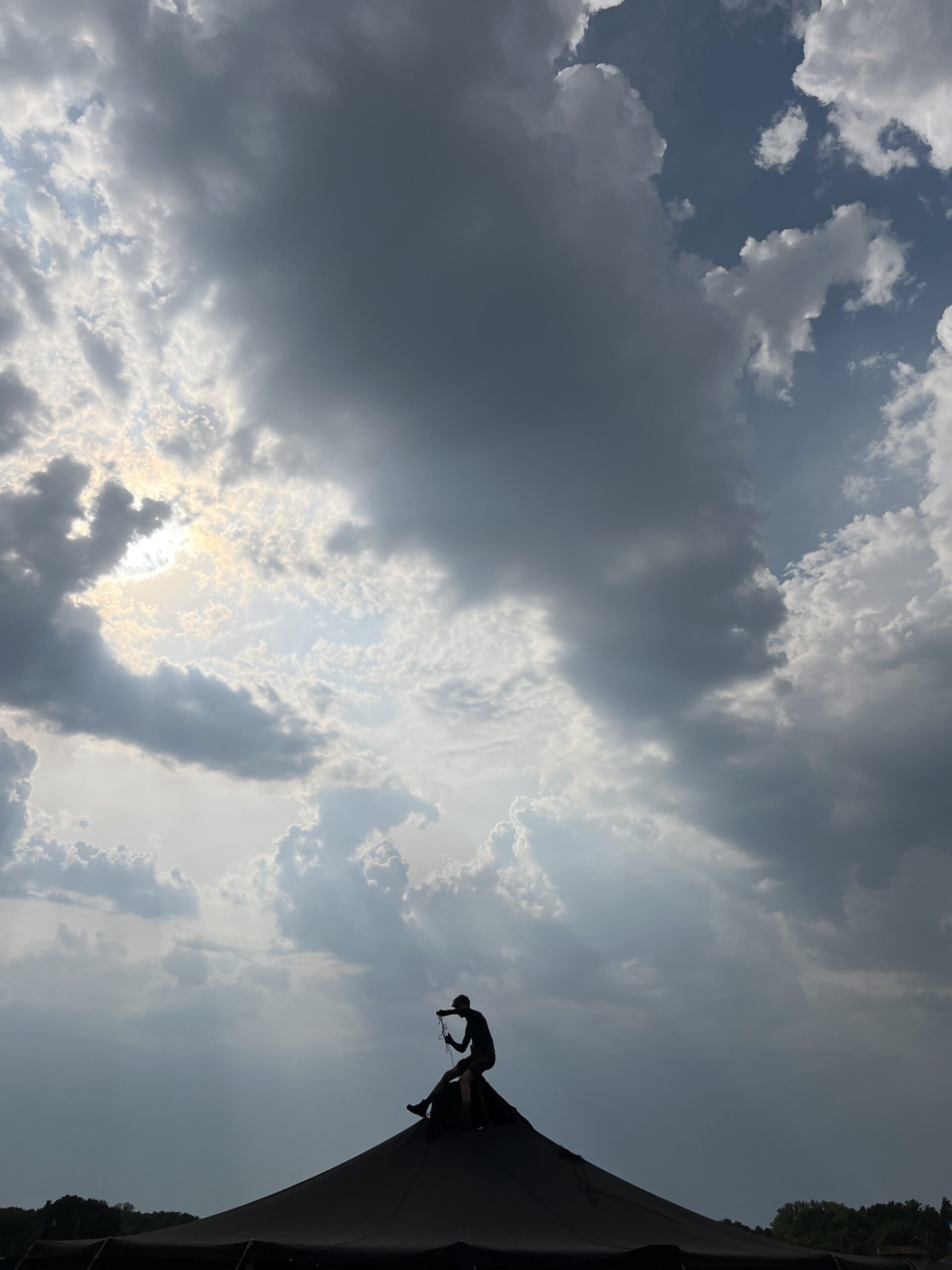 Ein Mensch sitzt oben im Dreibein einer Jurte und entfernt den Drachen, im Hintergrund türmen sich Wolken auf.