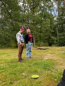 Zwei Teilnehmer*innen mit pinkfarbenen Fühlern auf dem Kopf stehen auf einer Wiese.